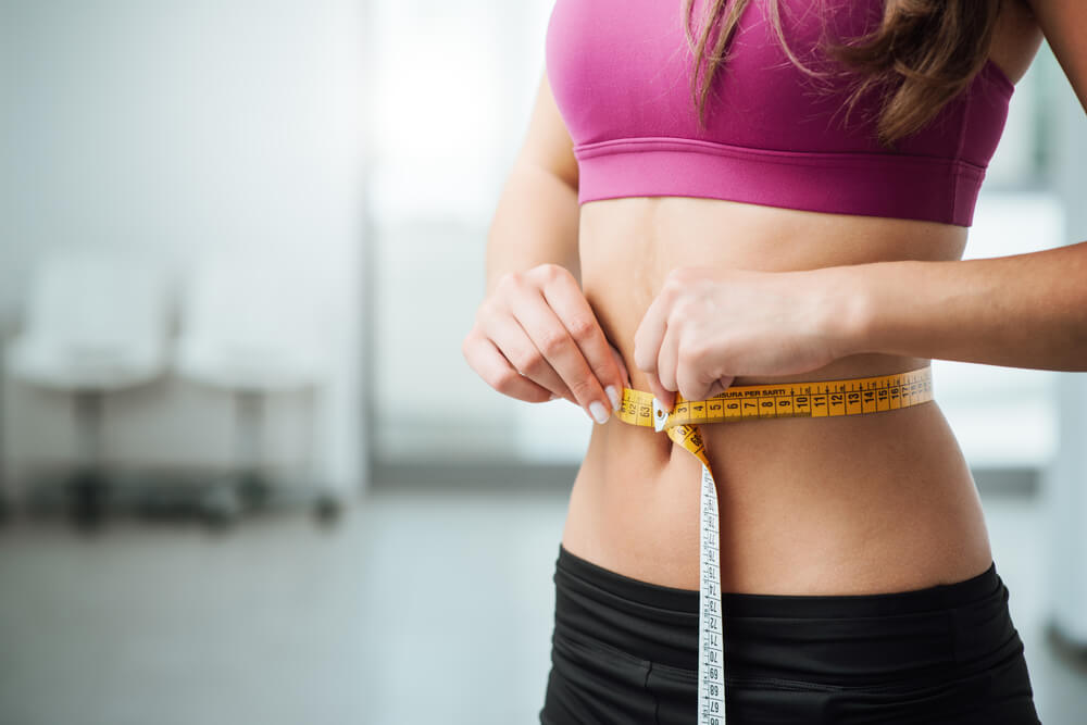 A slim woman is measuring her waist circumference.