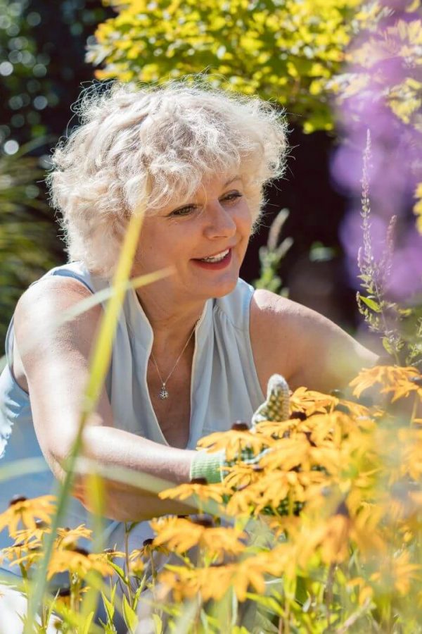 An elderly woman arranges flowers in her garden.