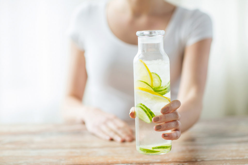 A woman is holding a glass jar with water and cucumber and lemon slices.