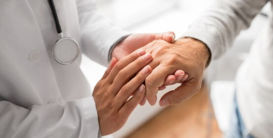 A doctor is compassionately holding the hand of an elderly patient.