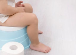 A little child is sitting on a blue potty and there is a toilet paper roll next to her.