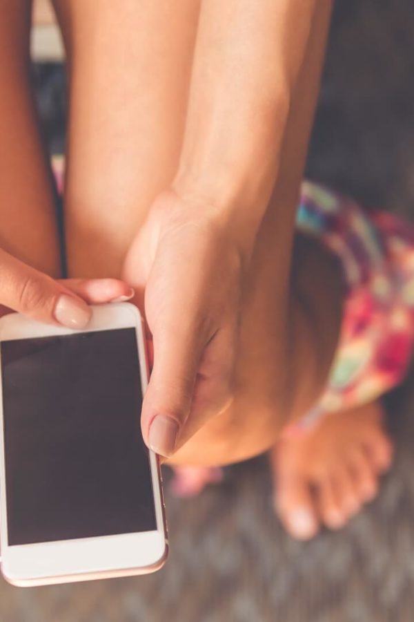 Eine Frau sitzt mit einem Telefon in der Hand auf der Toilette, weil sie Probleme mit einer langsamen und unregelmäßigen Verdauung hat.