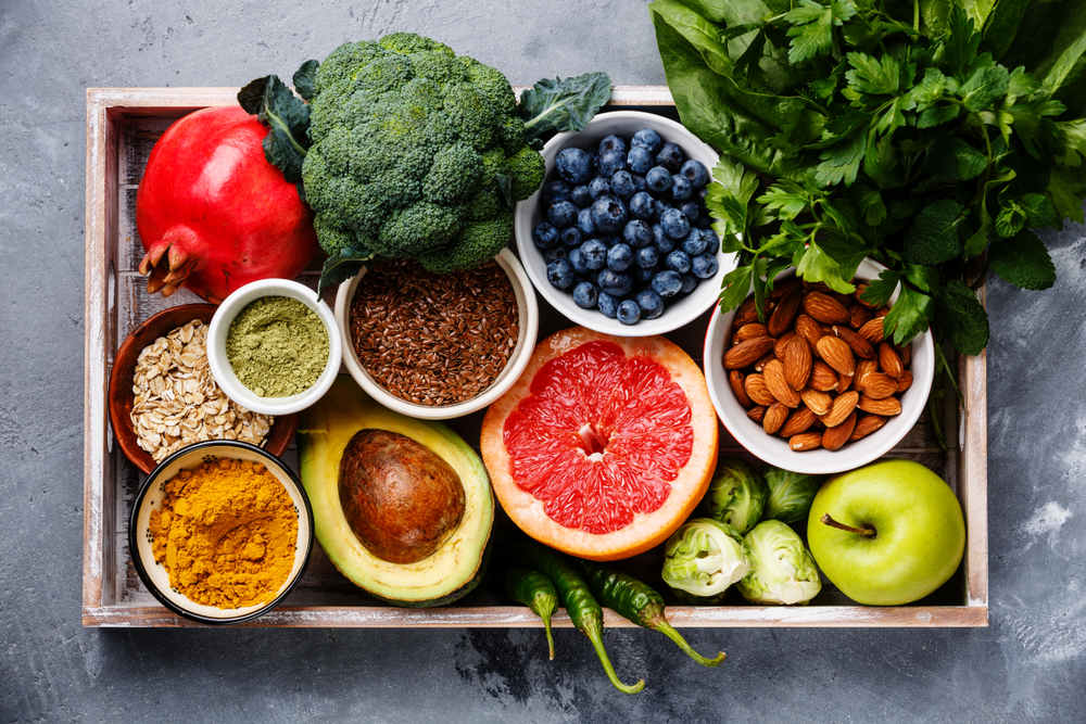 Healthy and nutrient-dense food on a wooden platter: fruit, vegetables, seeds, cereals, nuts, spices.