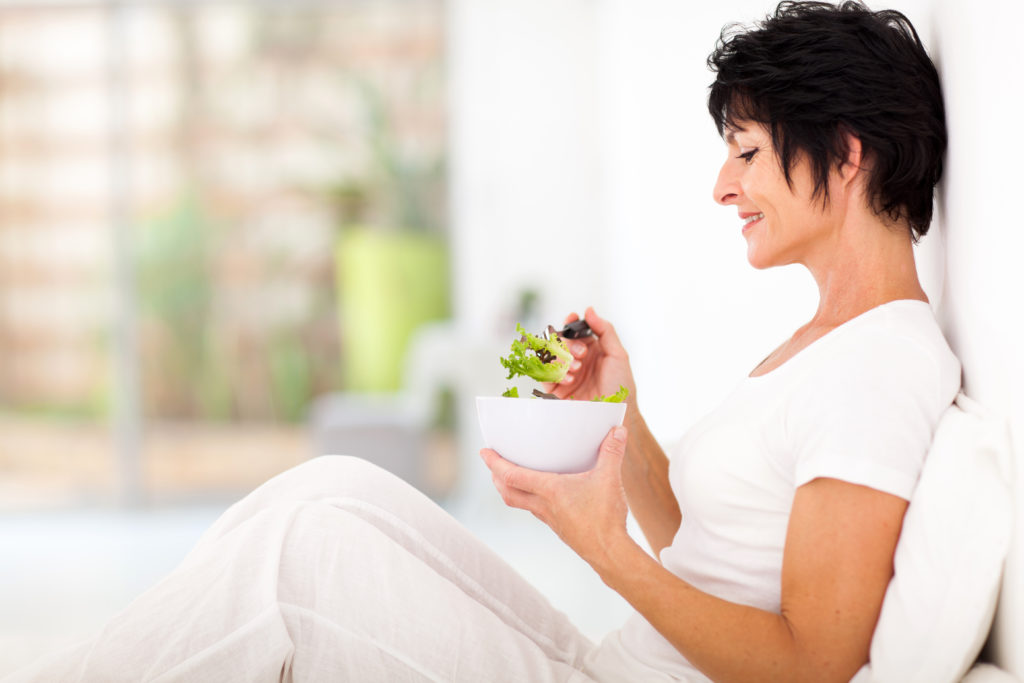 A healthy-looking elderly lady is eating a salad because she takes care of her healthy digestion.