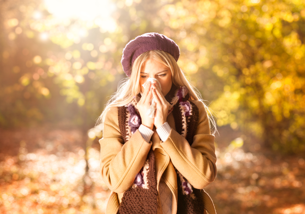 A young woman is wiping her nose with a tissue because she caught a cold due to a weakened immune system.