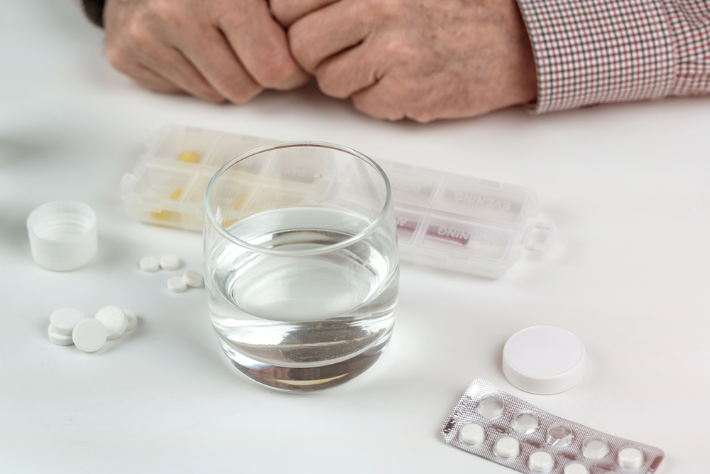 Many different pills on a white table and hands of an elderly gentleman.