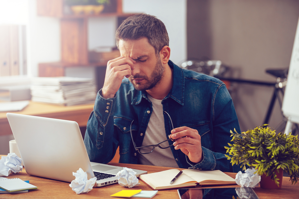 A stressed-out, tired young man is sitting at his office computer.