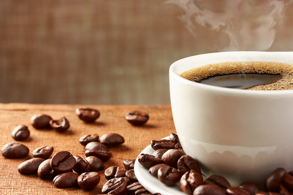 Hot coffee in a cup, coffee beans are next to it.