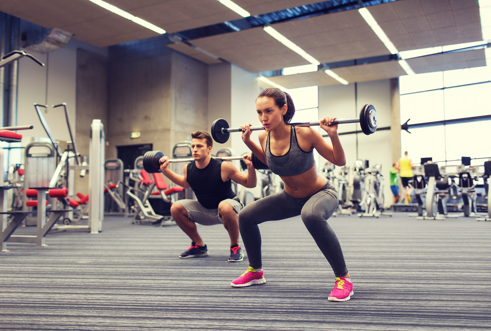 A young couple lifts weights in a squat position in the gym.